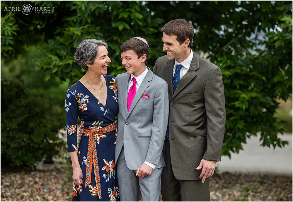 Bar Mitzvah Boy wearing bright pink tie laughs with his parents on the day of his bar mitzvah