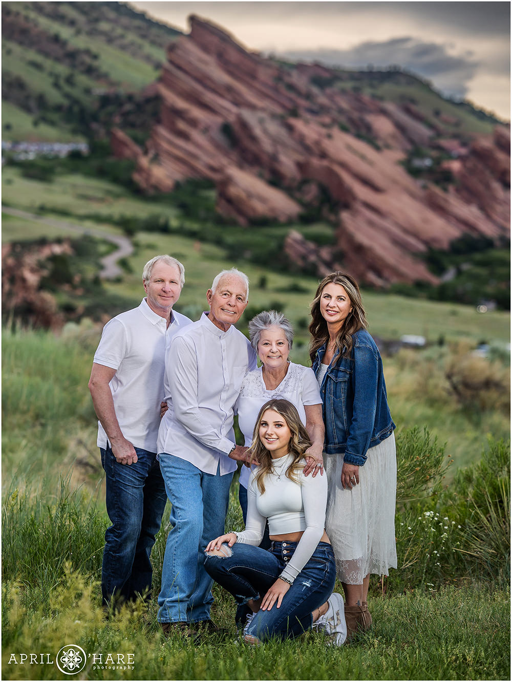 Beautiful summer family photo in the green grass with Red Rocks in the distance at East Mount Falcon in Colorado
