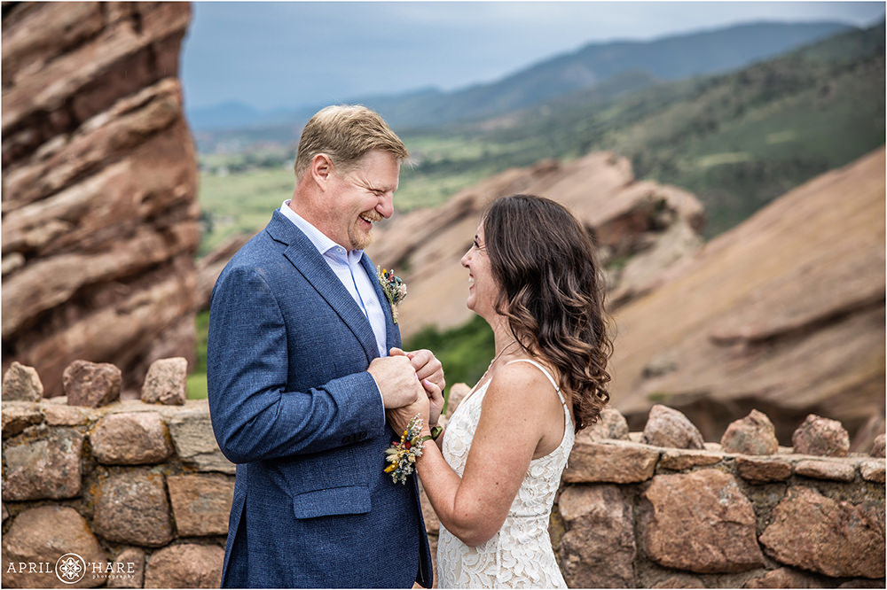 Bride and groom hold hands and laugh as they look into each other's eyes at the Red Rocks Trading Post backyard at their summer wedding