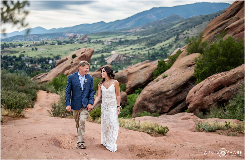 Bride and groom walk hand in hand along the Trading Post trail at their wedding at Red Rocks in Colorado