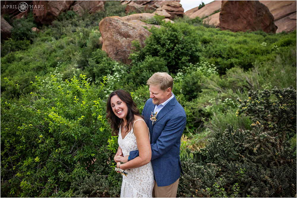 Bride and groom laugh with pretty green scenery behind them along a trail at Red Rocks in Colorado
