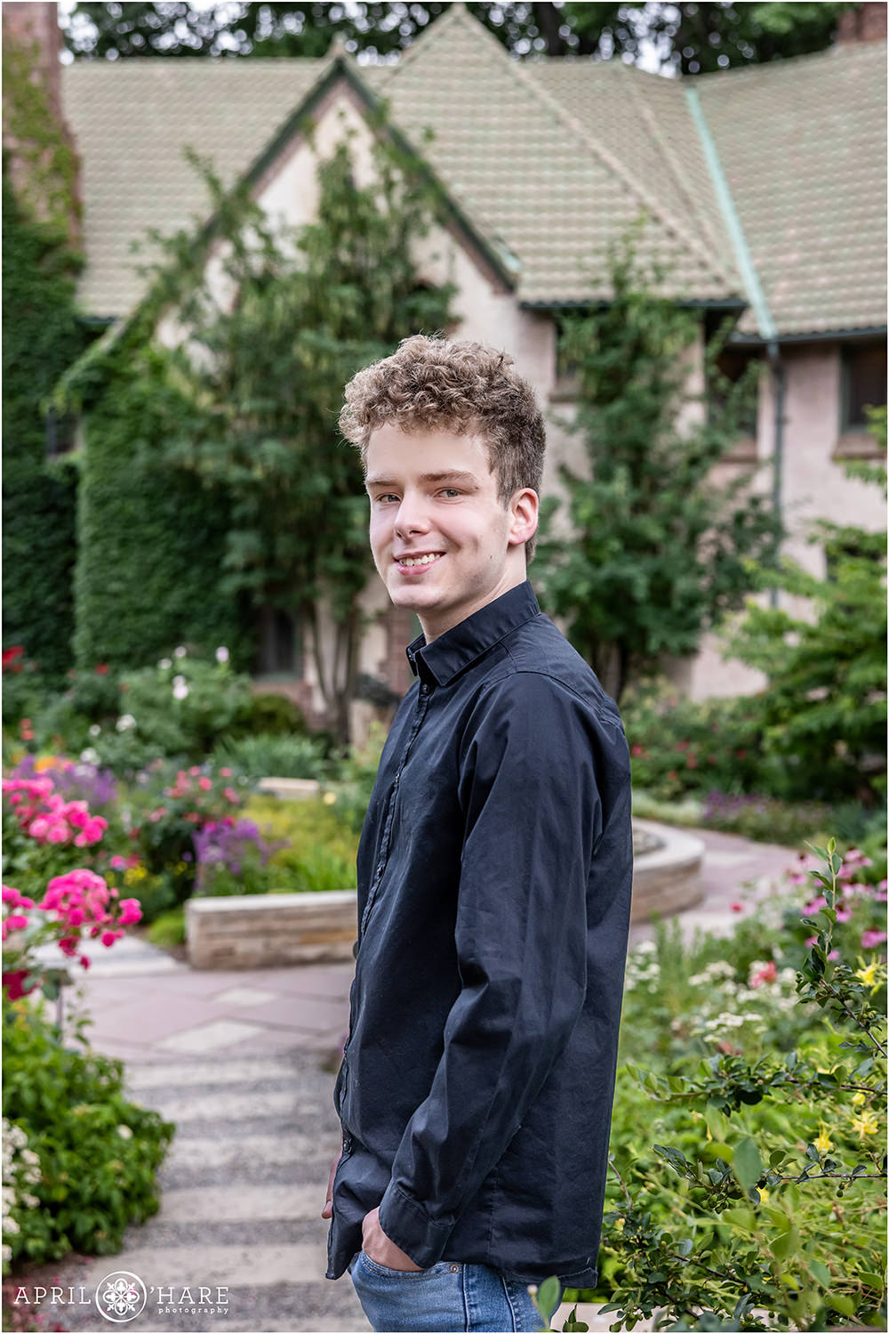 Handsome young senior wearing a black button down long sleeve shirt in a colorful garden setting in Denver