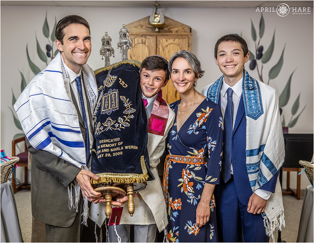 Family of 4 pose together while holding the Torah at B'nai Chaim in Lakewood CO
