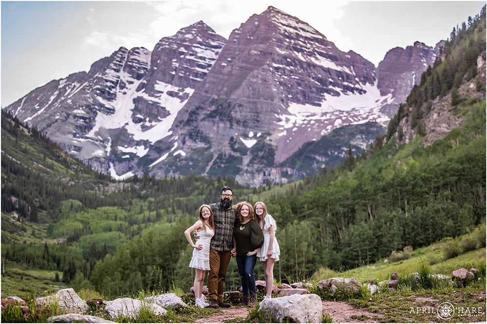 Family of four stand at Maroon Bells Amphitheater with the gorgeous mountain backdrop looming behind them during summer in Colorado