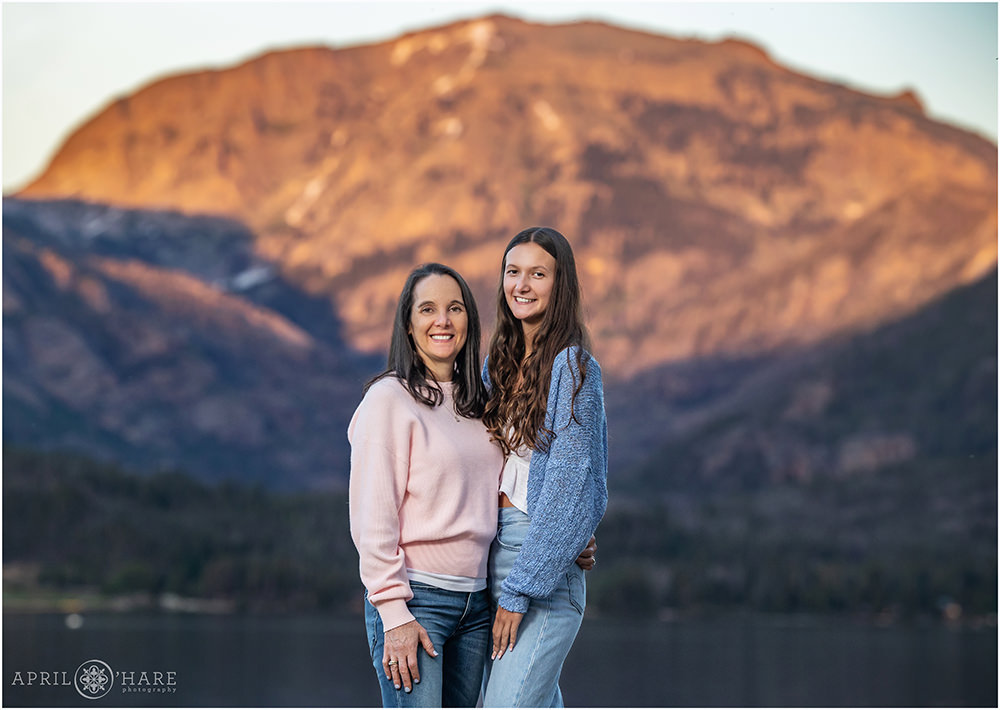 Mom with her teen daughter stand in front of a beautiful sunset mountain view at Point Park in Grand Lake Colorado