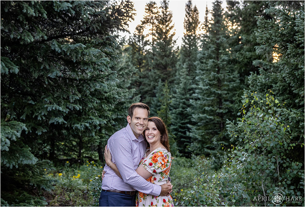 Couple snuggle in a pretty green forest during summer in Colorado
