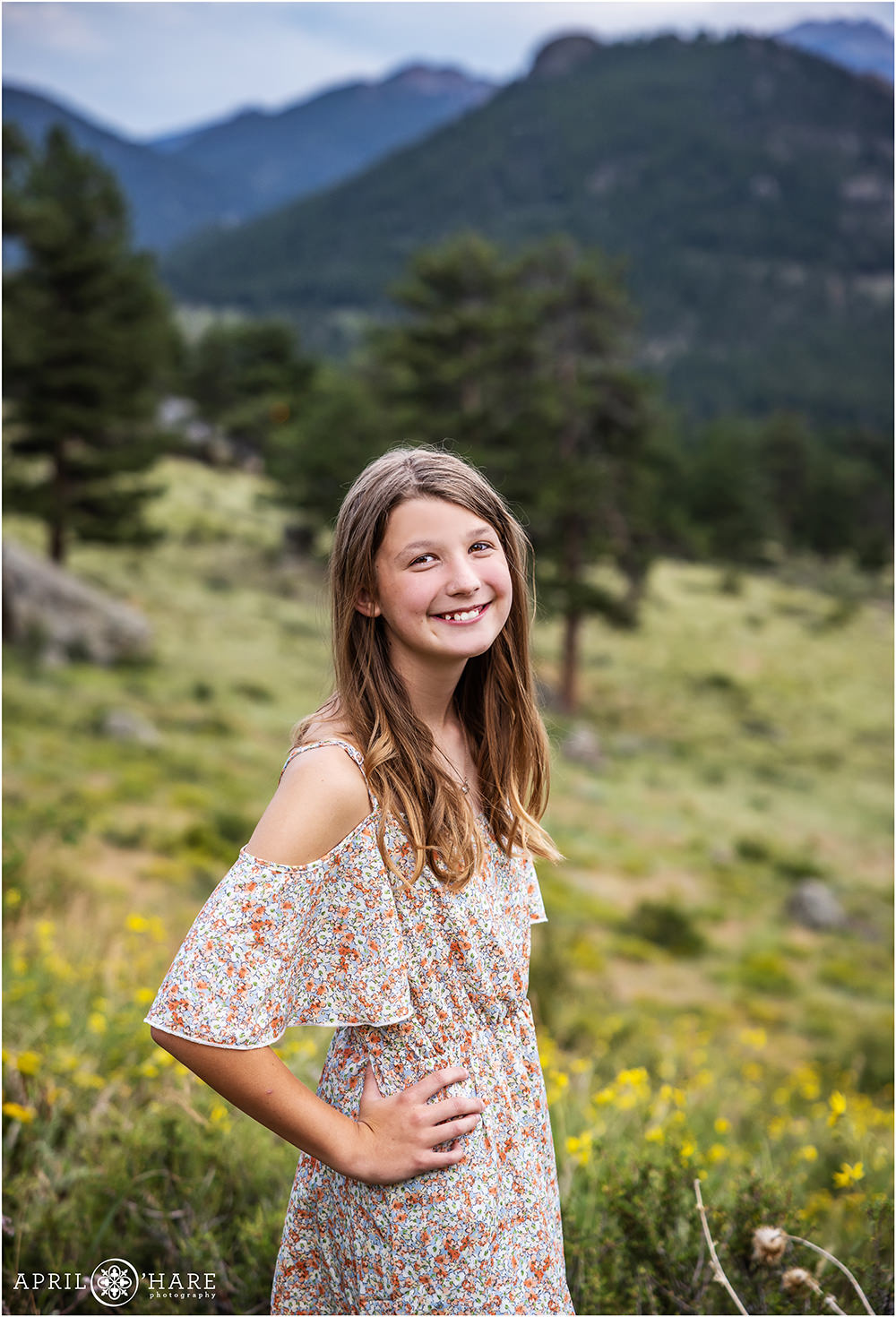 Girl stands in a field with yellow wildflowers with mountain backdrop at Rocky Mountain National Park in Estes Park Colorado