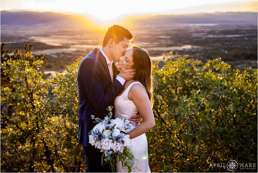 Romantic photo of groom kissing his bride's cheek in front of a pretty sunset backdrop in Colorado