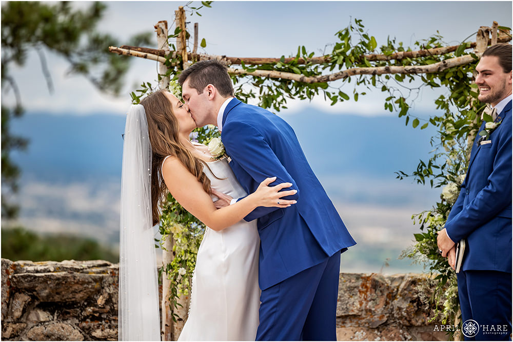Groom kisses his bride at the end of their wedding ceremony with mountain backdrop at Castle wedding in Colorado
