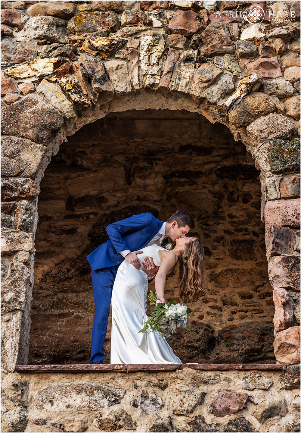 Groom dips his bride in an archway at Cherokee Ranch and Castle in Sedalia CO