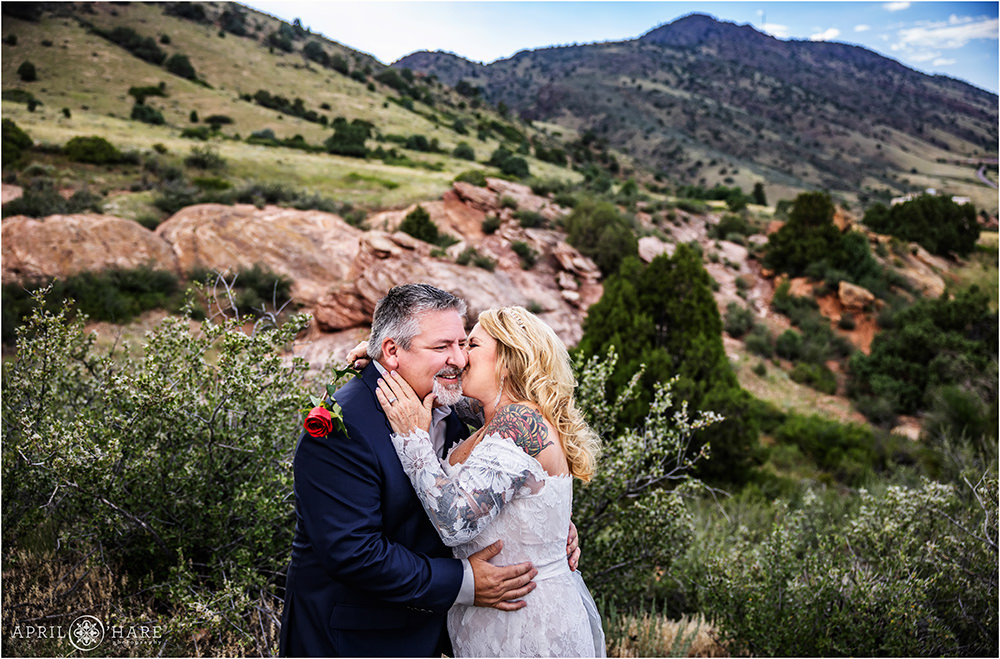Sweet couple snuggle and kiss in front of a pretty red rocks view at East Mount Falcon Trailhead During Summer Elopement