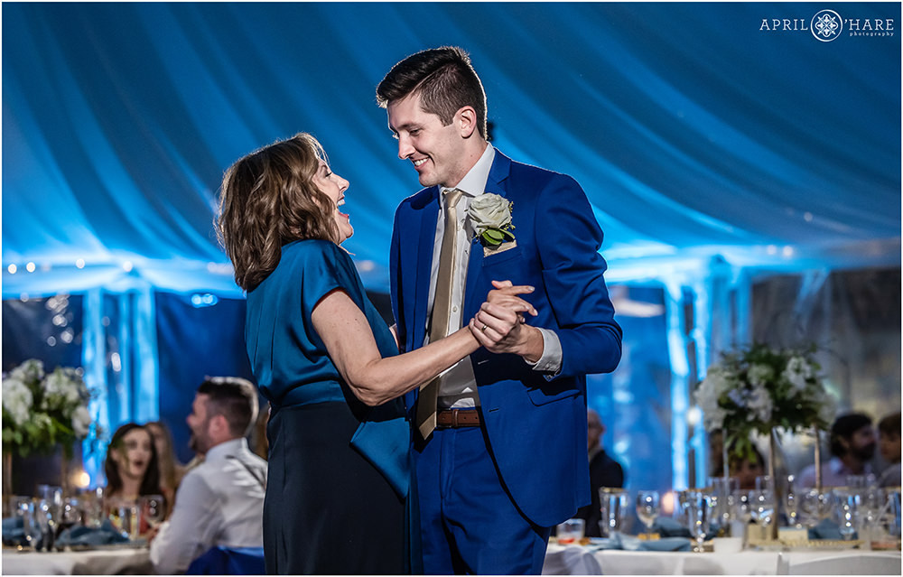 Groom dancing with his mom with blue light tent backdrop in Colorado