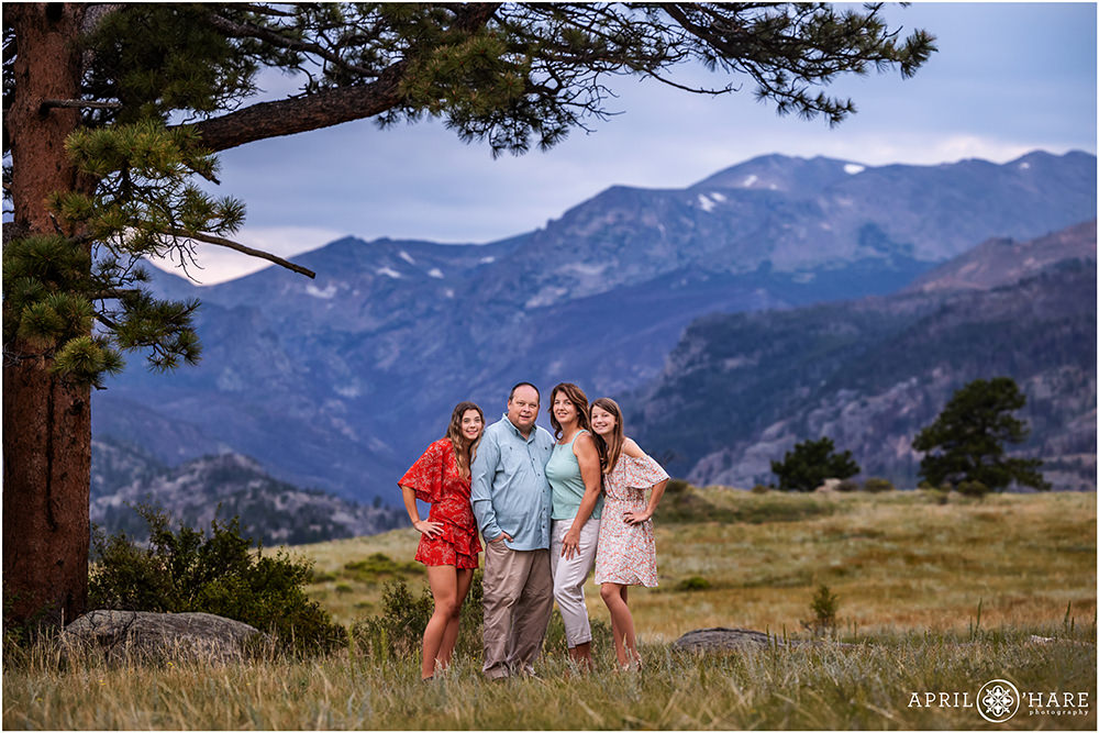 Family of four with a gorgeous mountain backdrop and a huge evergreen tree at Rocky Mountain National Park