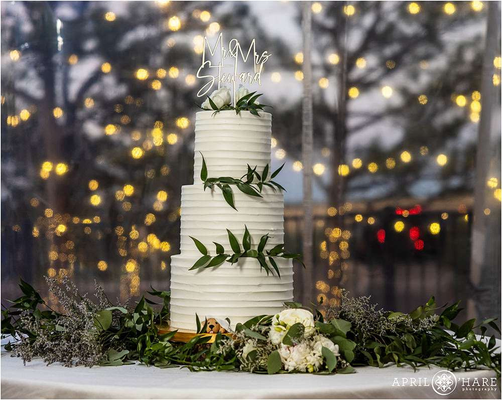 Pretty three tiered white wedding cake with twinkle light backdrop at Castle Wedding in Colorado