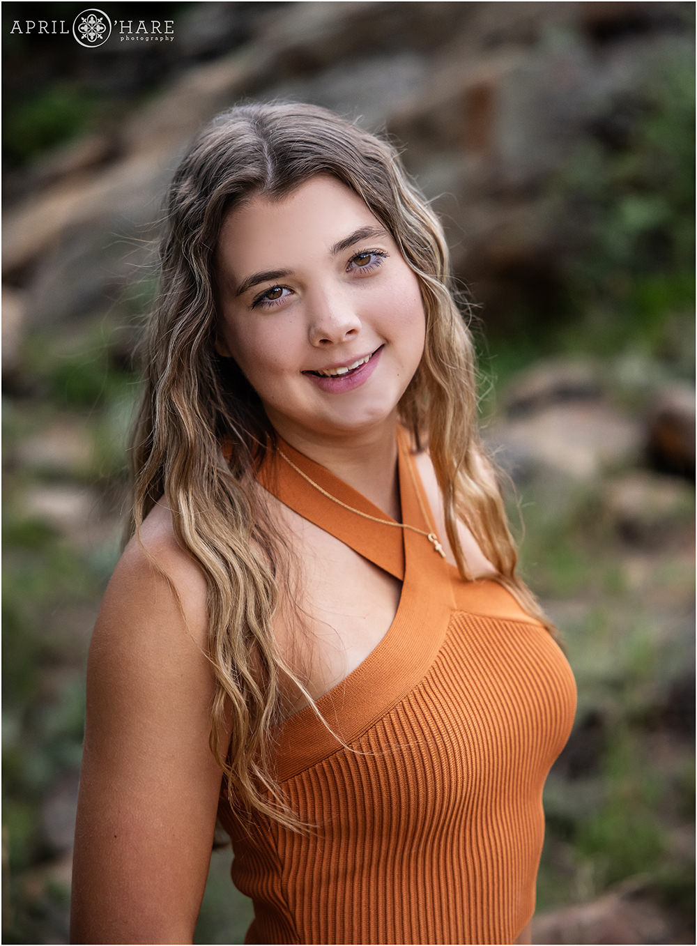 Colorado senior portrait for a young lady wearing rust orange tank top in front of a rock in Rocky Mountain National Park