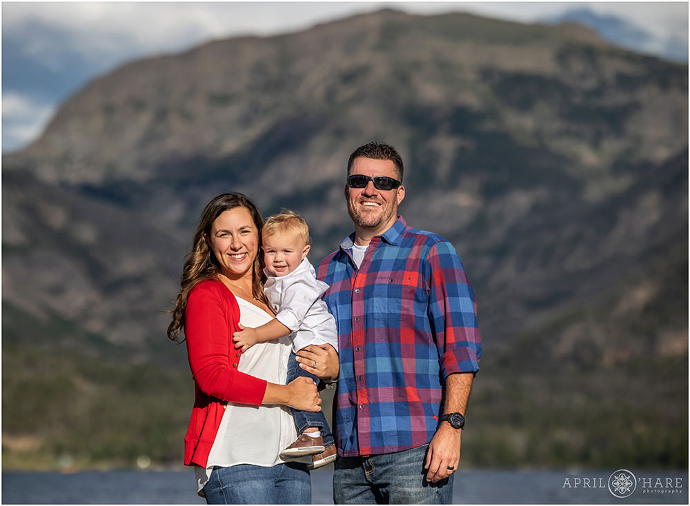 A family of 3 with a young son pose in front of the mountain view in Grand Lake Colorado