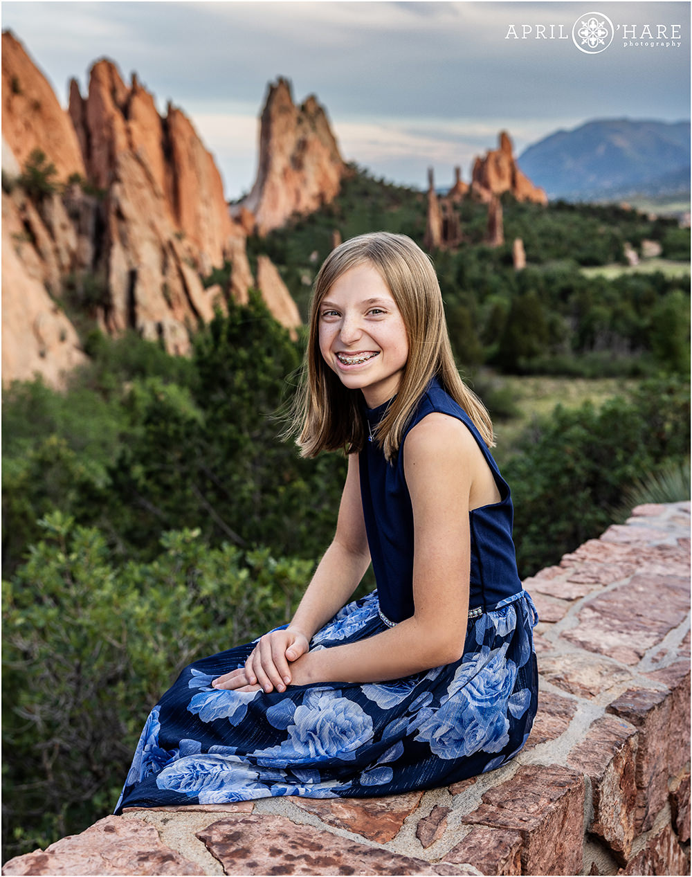 Girl wearing a blue dress with floral pattern sits on a ledge at Garden of the Gods in Colorado Springs