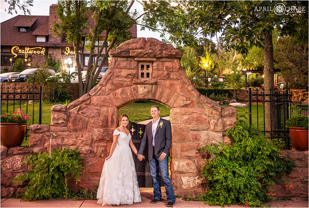 Bride and groom hold hands in front of the sandstone gate at Craftwood Inn in Manitou Springs CO