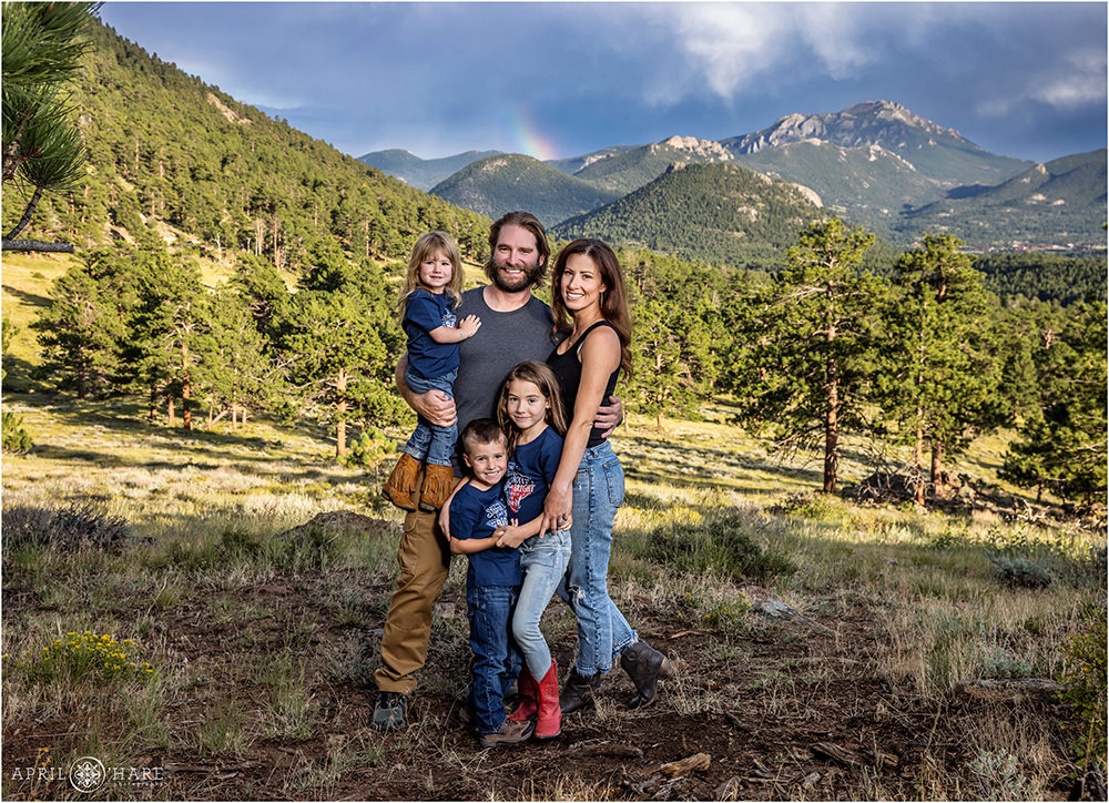 Family of 5 with young children stand in front of a mountain backdrop with a rainbow at Rocky Mountain National Park in Colorado