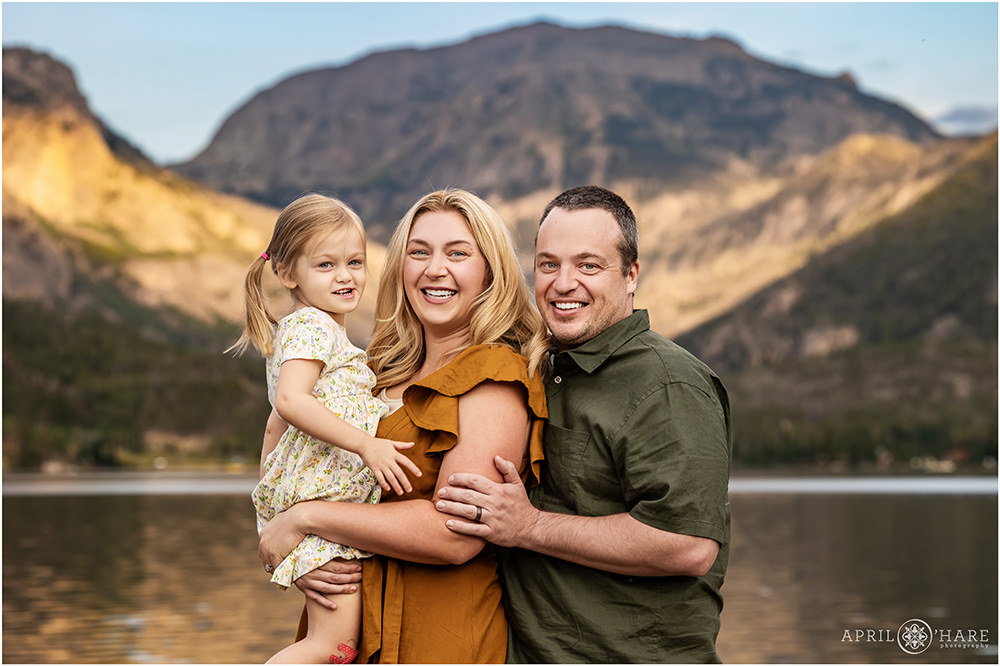 Family of three with a young toddler daughter pose in front of a pretty mountain backdrop in Colorado