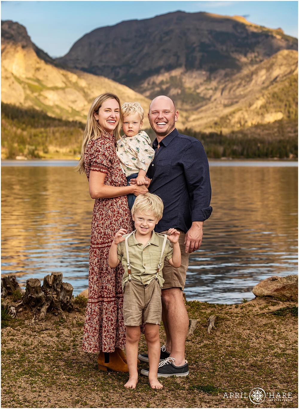 Family of four with two young sons pose in front of a mountain backdrop at Point Park in Grand Lake
