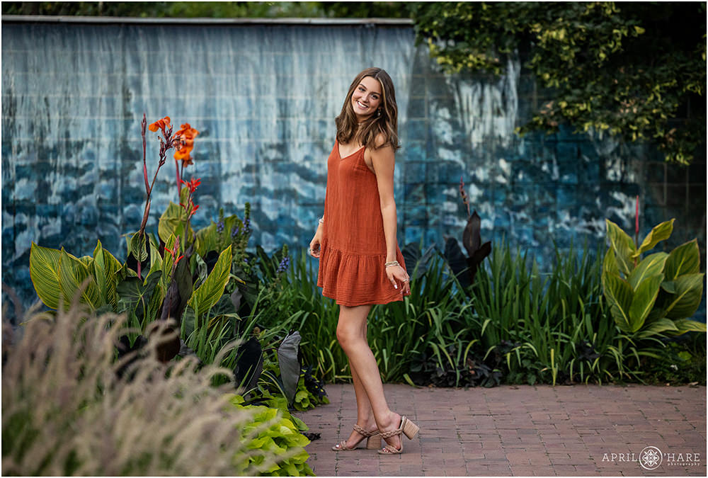 Senior girl wearing a cute orange dress with blue fountain backdrop at Denver Botanic Gardens in Colorado