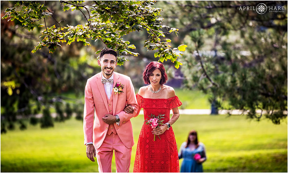 Groom wearing a pink suit walks his mom down the aisle at Grant-Humphreys Mansion in Denver