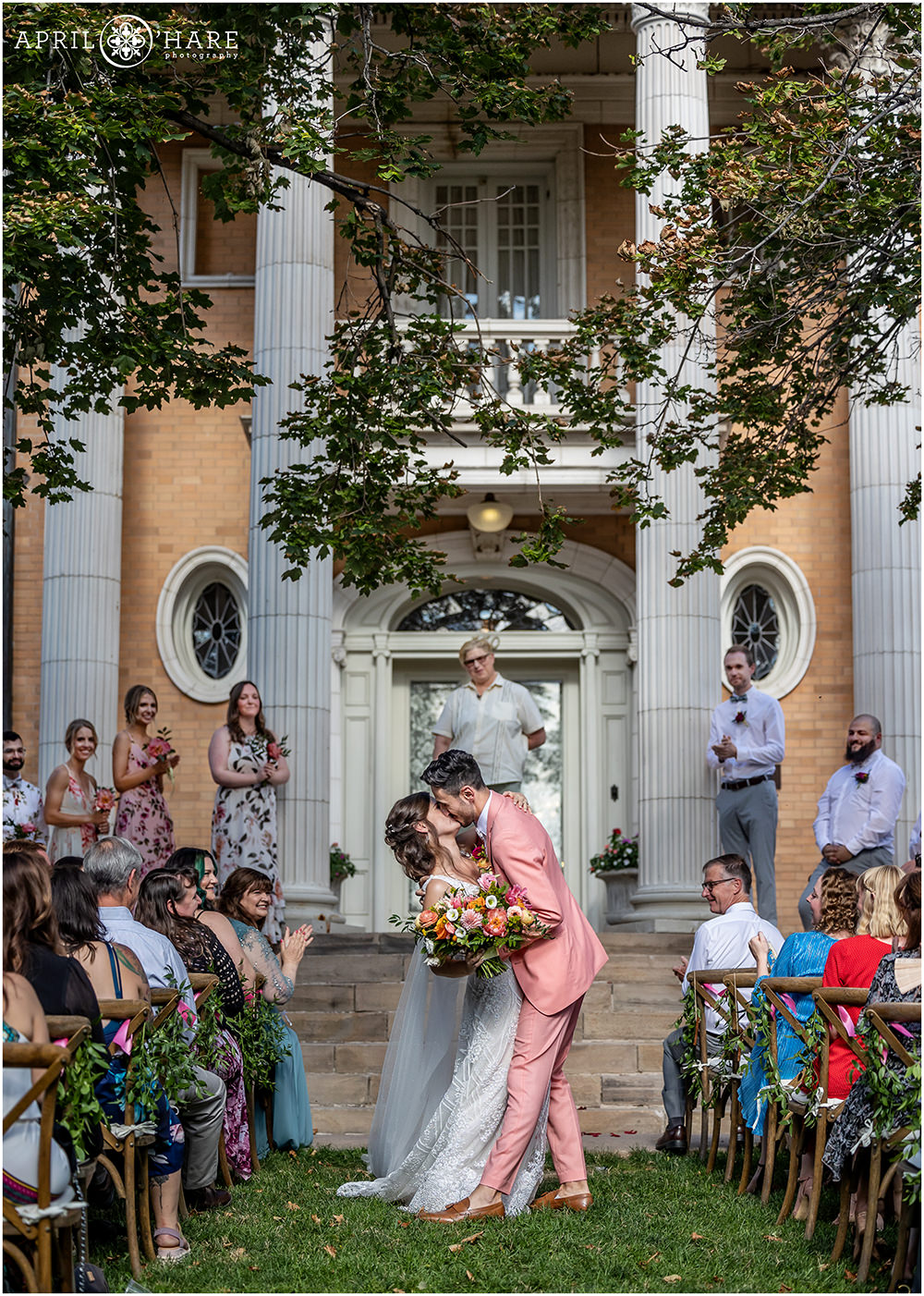 Groom kisses his bride as they exit their wedding ceremony at the Grant Humphreys Mansion in Denver