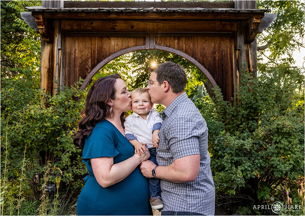 Cute toddler boy gets a kiss from both of his parents in front of the circle arch at Denver Botanic Gardens