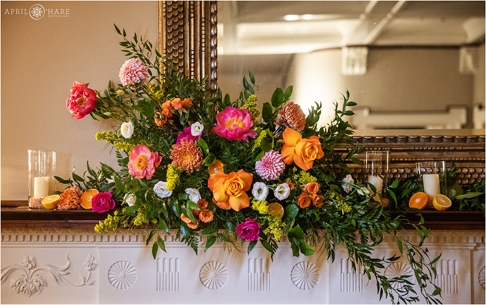Beautiful orange, pink, tangerine citrus colored florals decorate the mantel of the great room fireplace at Grant-Humphreys Mansion in Denver