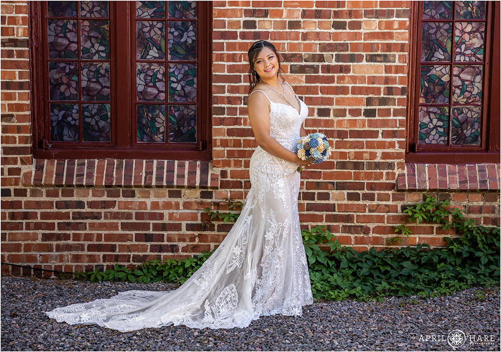 Bride poses in front of red brick wall with stained glass windows at Wellshire Event Center