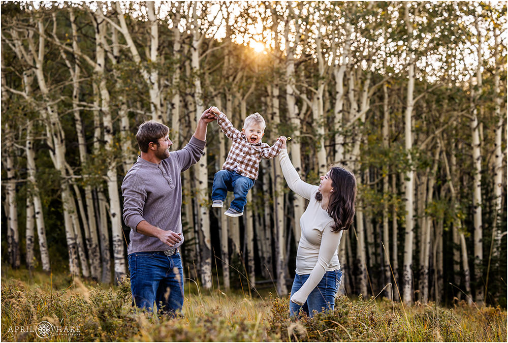 Mom and dad swing their cute son in the air with aspen tree backdrop in Evergreen Colorado