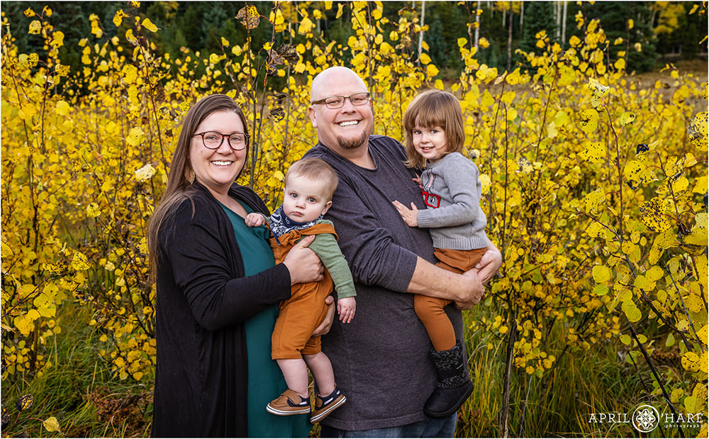 Family of four with two cute children in the aspen leaves during fall in Colorado