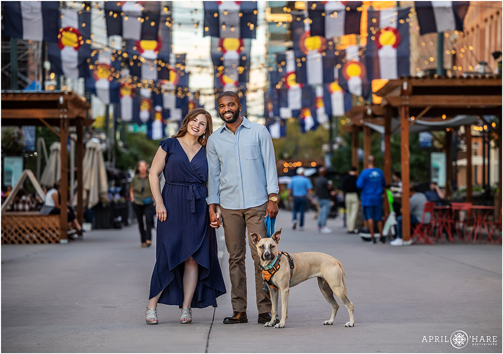 Engagement photo at Larimer Square with Colorado flags hanging overhead with their dog