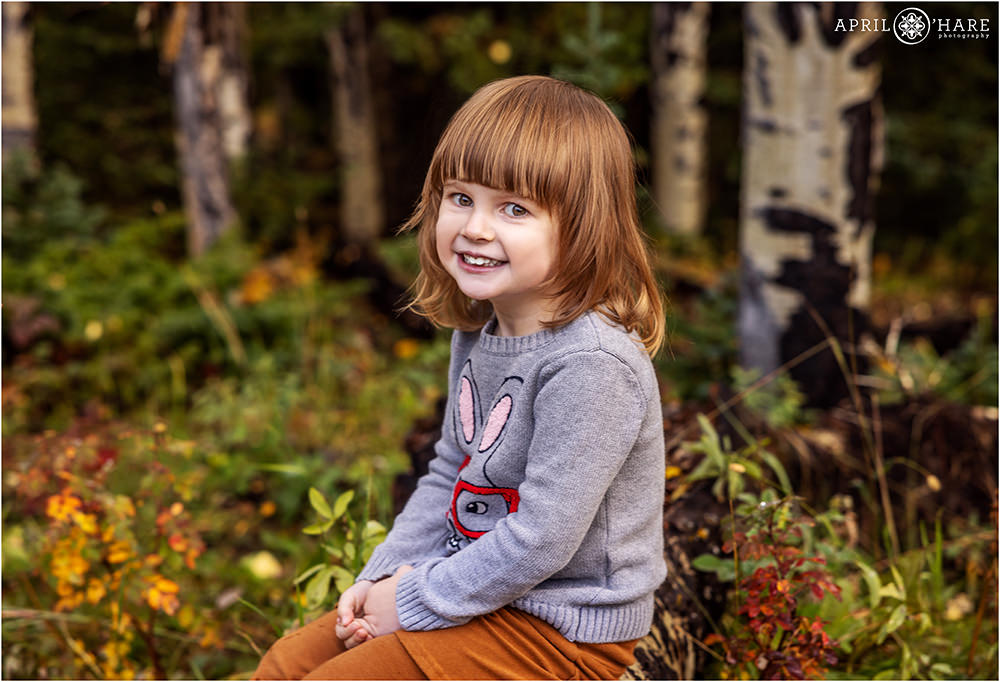 Cute girl sits on a log with pretty fall color surrounding her in Evergreen Colorado