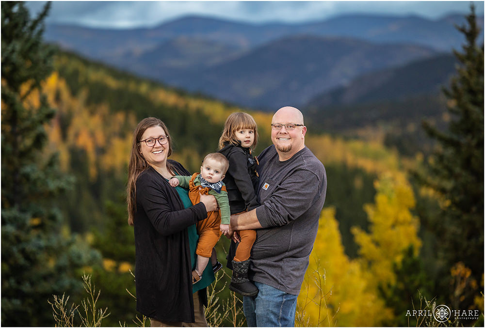 Family of four with two young children are photographed in front of a pretty mountain backdrop with yellow aspen dotting the landscape in Colorado