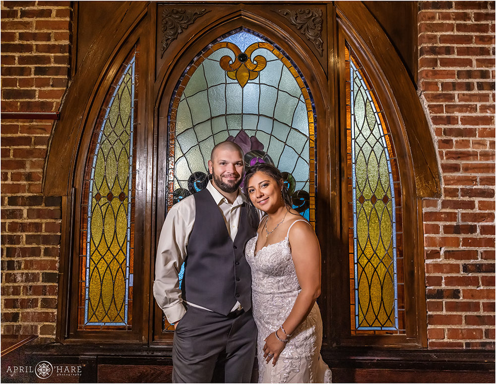 Bride and groom portrait in front of a pretty arched stained glass window at Wellshire Event Center in Denver