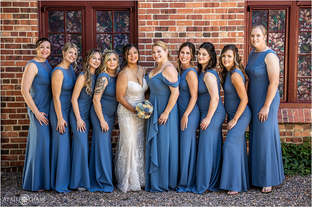 Bride with her best friends on her wedding day in front of a brick wall with stained glass windows at Wellshire Event Center