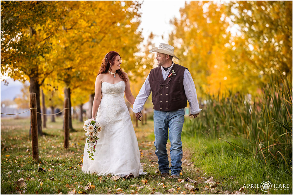 Couple wearing their wedding attire walk hand in hand with the fall color behind them at Anderson Farms in Erie Colorado