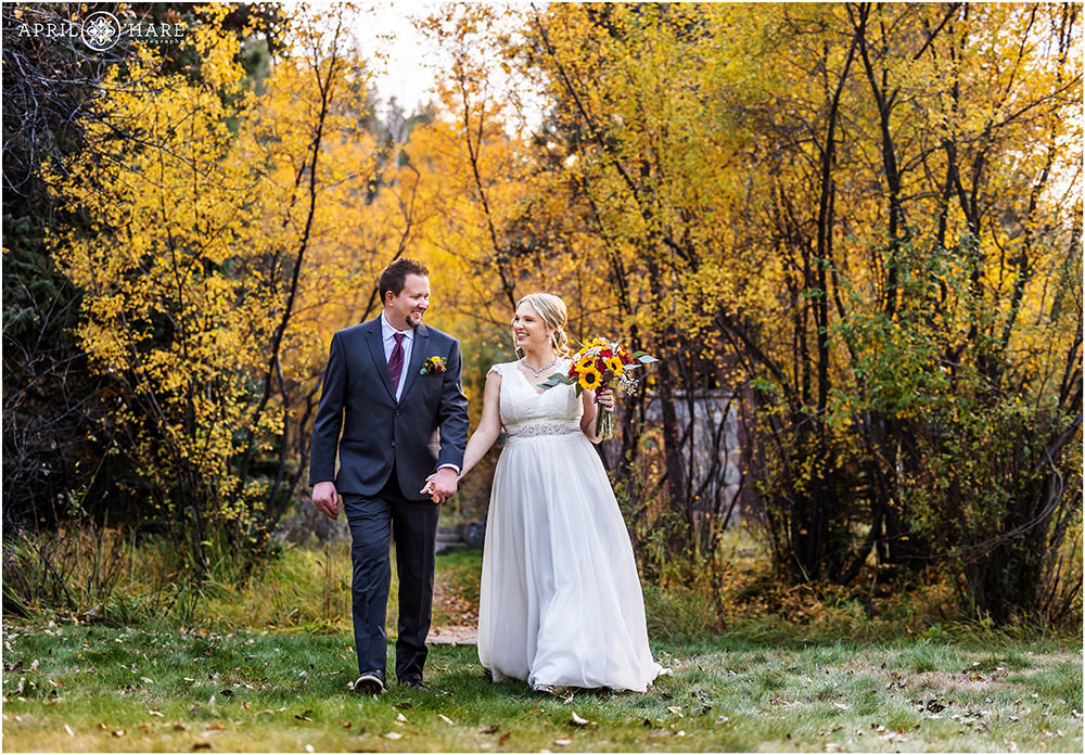Bride and groom walk across the lawn with fall color behind them at Romantic Riversong Inn