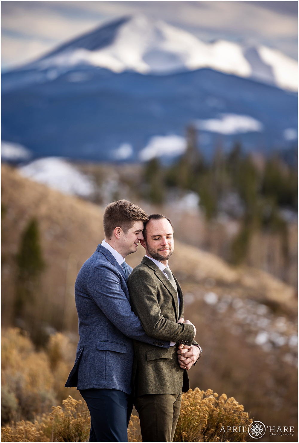 Two grooms snuggle on their wedding day with a large mountain in the backdrop