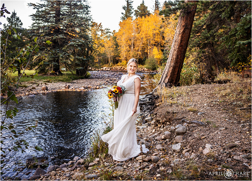Bride stands next to river at Romantic Riversong Inn in Colorado