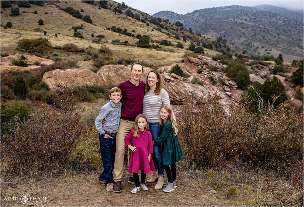 Cute family of 5 pose for a photo with red rocks backdrop at East Mount Falcon Trailhead in Morrison CO