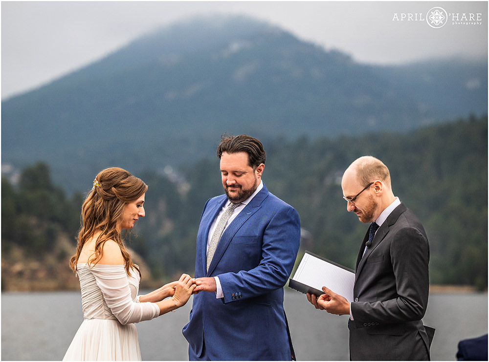 Bride puts a ring on her groom's finger at their lakeside wedding at the Evergreen Lake House