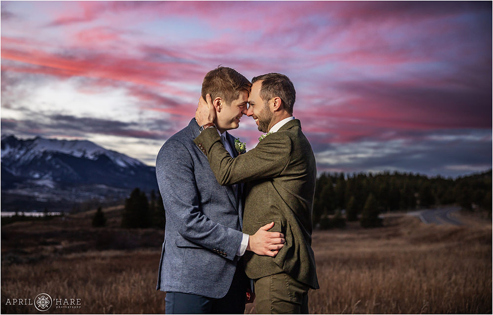 Two grooms embrace with a pretty pink sunset backdrop in Colorado