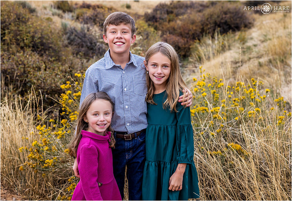 Three young siblings pose for a portrait together in the fall color at East Mount Falcon Trailhead