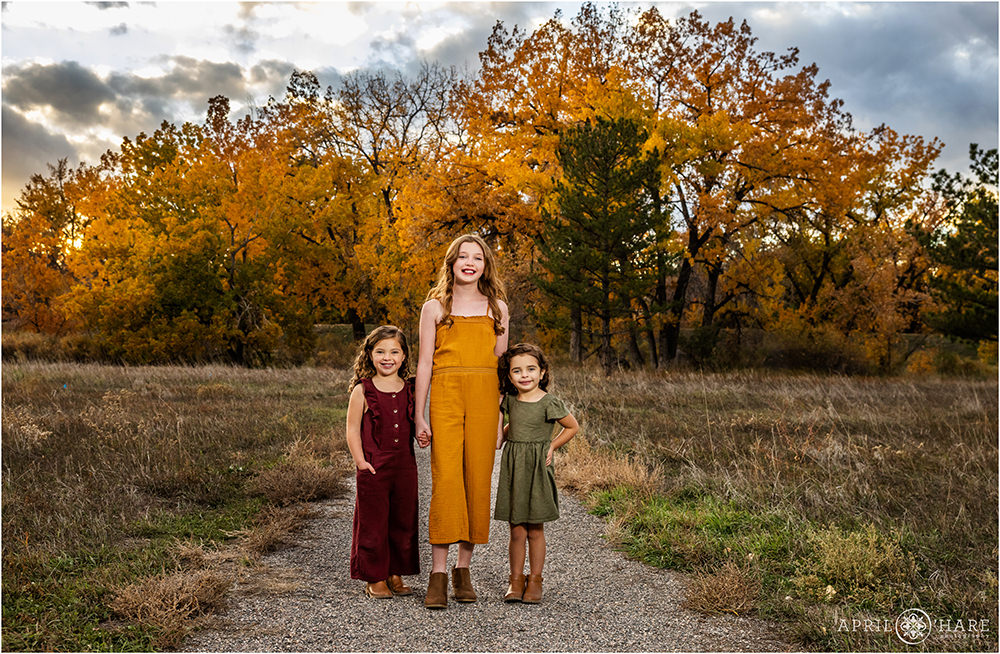 Cute photo of three sisters holding hands with gorgeous fall color backdrop at James Bible Park