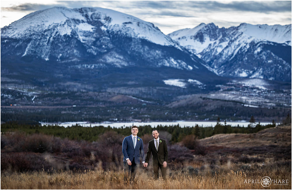 Grooms hold hands in front of an epic mountain backdrop in Colorado