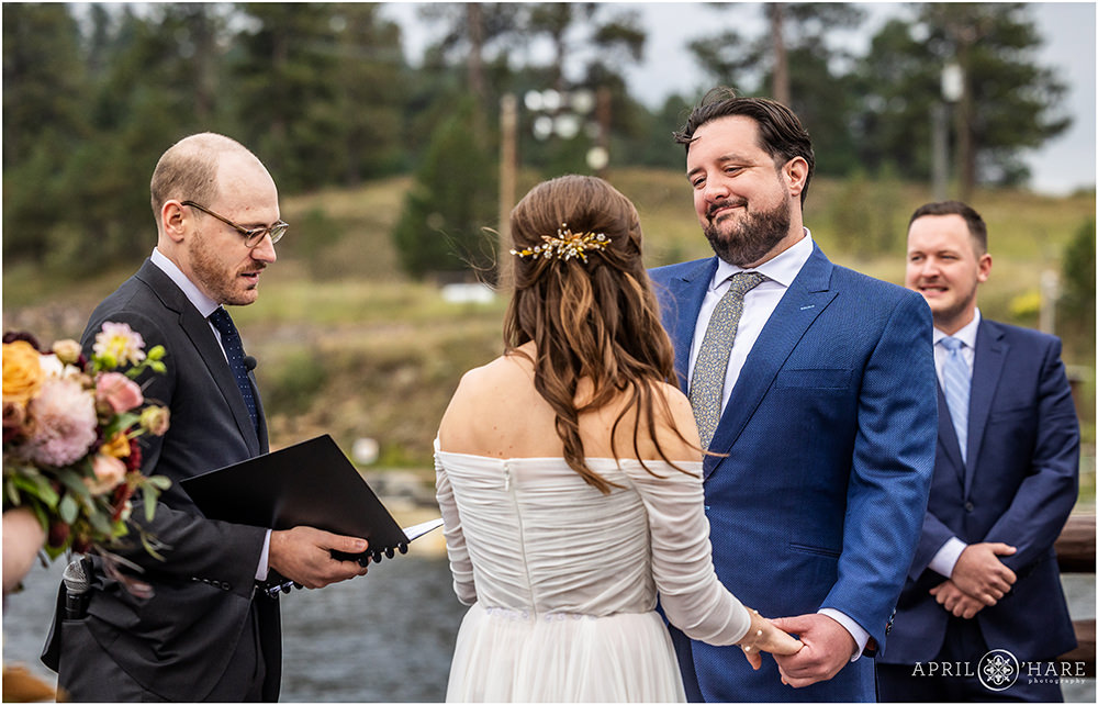 Groom smiles at his bride as they get married next to the lake at Evergreen Lake House