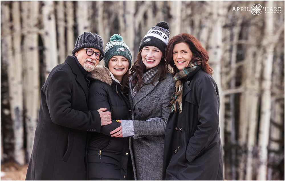 A family of four all bundled up during winter get a portrait together in front of an Aspen tree grove in Evergreen CO
